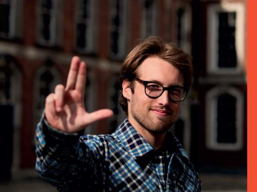 A student wearing glasses holds their hands up with the Laker for a Lifetime symbol.